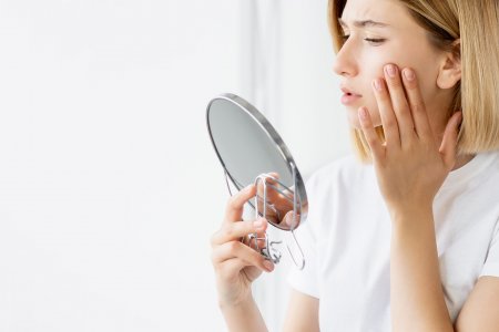 A woman examining her acne-prone skin in the mirror, pleased with the improvement by following clear skin steps.